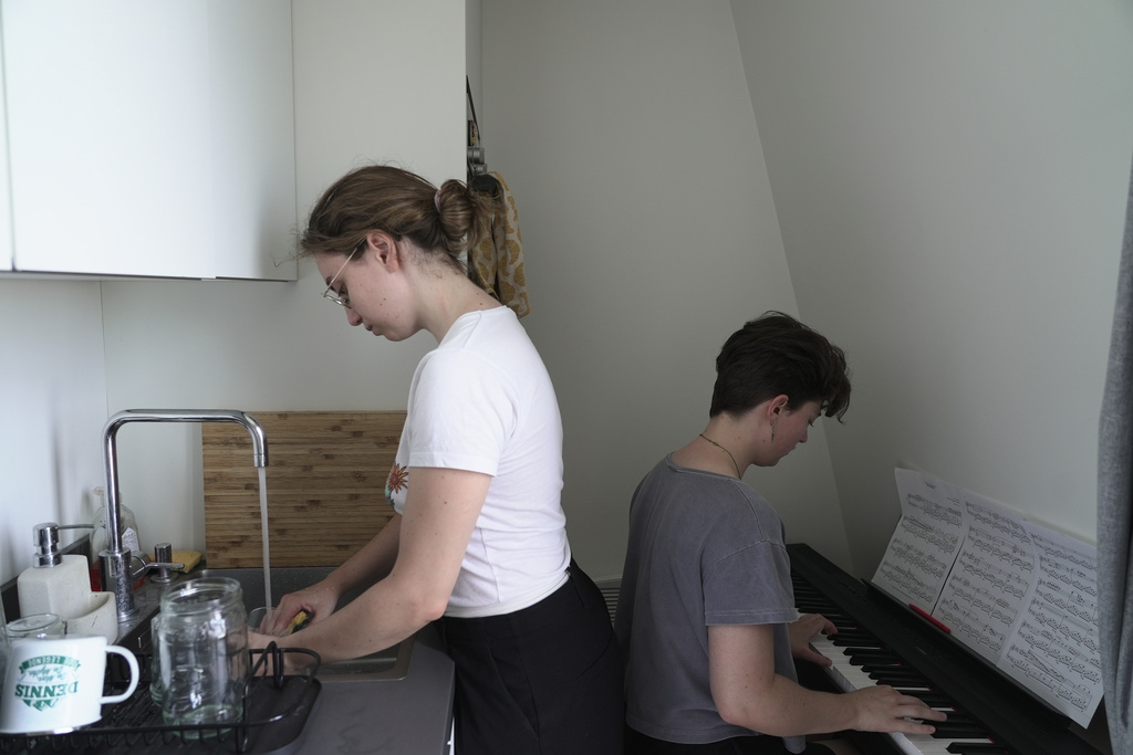 Amelie Kenney, right, plays piano in the attic apartment she shares with her partner Francesca Pilia, in Paris, Wednesday, June 24, 2026. (AP Photo/John Leicester)