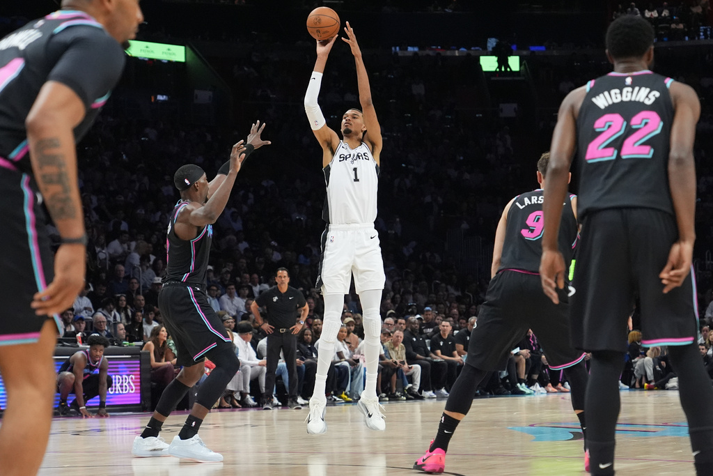 San Antonio Spurs forward Victor Wembanyama (1) shoots a three-point basket over Miami Heat center Bam Adebayo (13) during the first half of an NBA basketball game, Monday, March 23, 2026, in Miami. (AP Photo/Lynne Sladky)