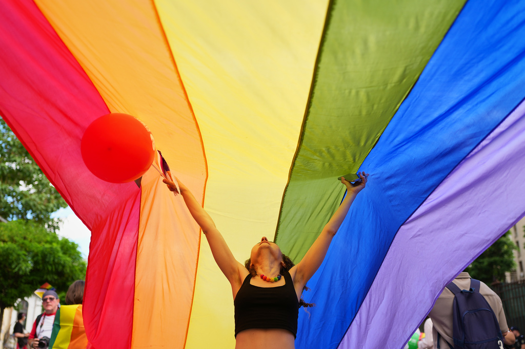 A person gestures under a rainbow flag during the Bucharest Pride Parade, in Bucharest, Romania, Saturday, June 13, 2026. (AP Photo/Andreea Alexandru)