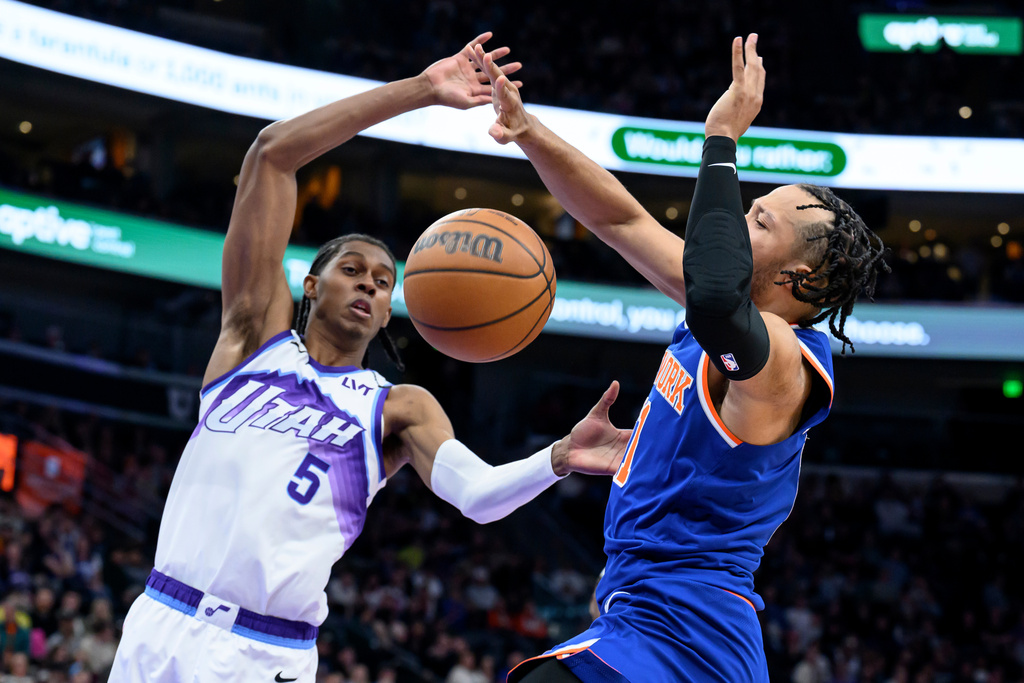 Utah Jazz forward Cody Williams, left, and New York Knicks guard Jalen Brunson, right, battle for possession of the loose ball during the first half of an NBA basketball game, Wednesday, March 11, 2026, in Salt Lake City. (AP Photo/Tyler Tate)