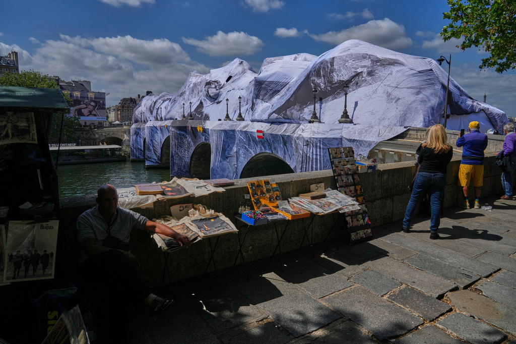 People take pictures of "The Pont Neuf Cave," an inflated art installation by French street artist JR, on Paris' oldest bridge, the Pont Neuf, Thursday, May 21, 2026, which will be open to the public from June 6-28. (AP Photo/Michel Euler)