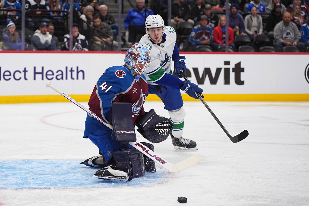 Colorado Avalanche goaltender Scott Wedgewood, front, deflects a shot from Vancouver Canucks center Linus Karlsson in the second period of an NHL hockey game, Tuesday, Dec. 2, 2025, in Denver. (AP Photo/David Zalubowski)
