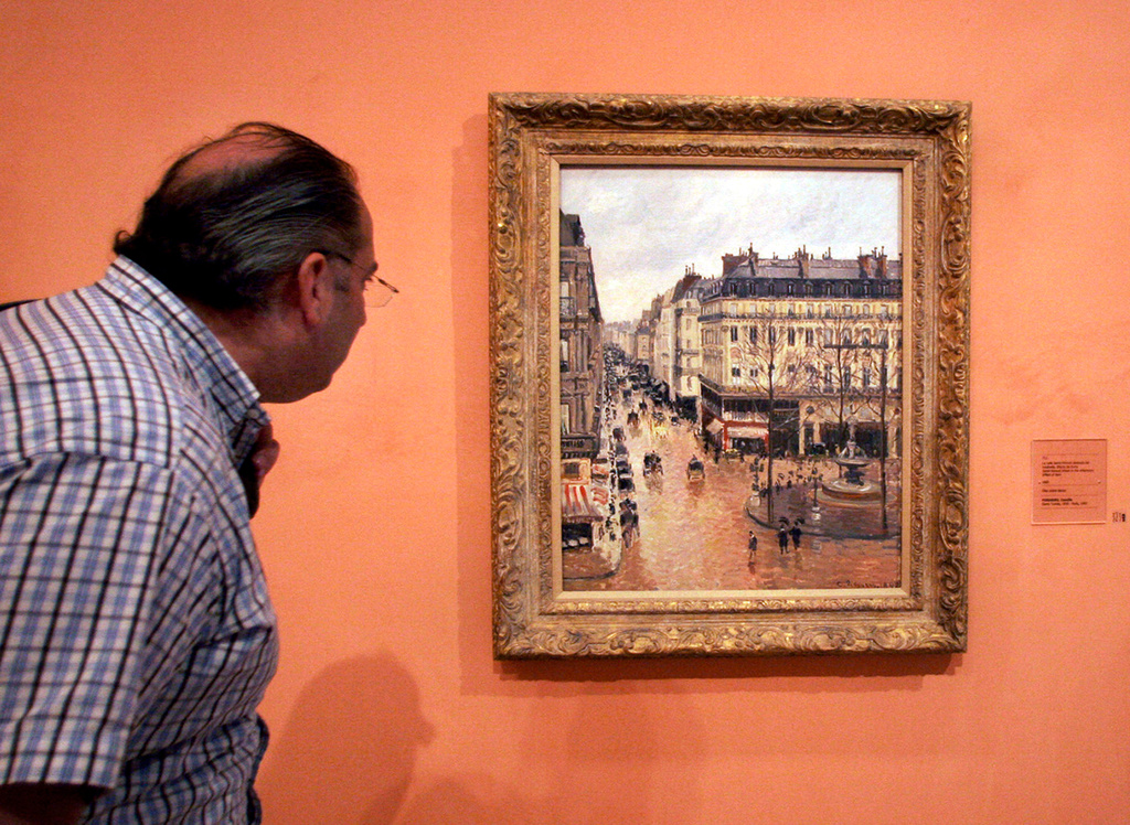 FILE - A visitor views the Impressionist painting, "Rue St.-Honore, Apres-Midi, Effet de Pluie," ("Rue Saint-Honoré in the Afternoon, Effect of Rain") painted in 1897 by Camille Pissarro, on display in the Thyssen-Bornemisza Museum in Madrid on May 12, 2005. (AP Photo/Mariana Eliano, File)