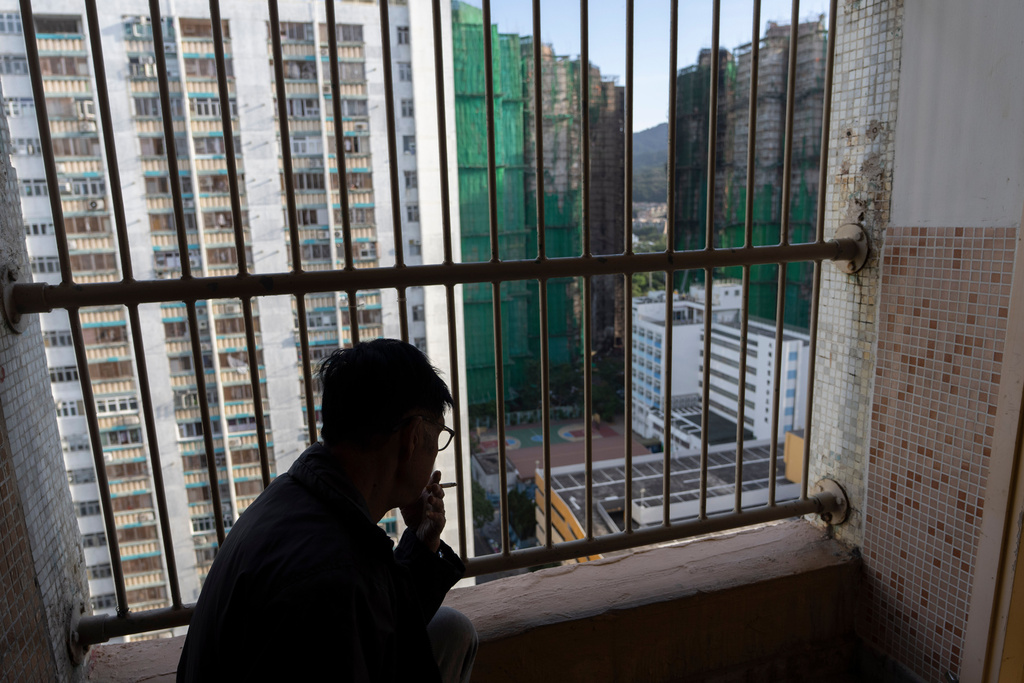 A resident smokes as he looks out towards buildings burnt after a deadly fire that started Wednesday at Wang Fuk Court, a residential estate in the Tai Po district of Hong Kong's New Territories, Friday, Nov. 28 2025. (AP Photo/Ng Han Guan)