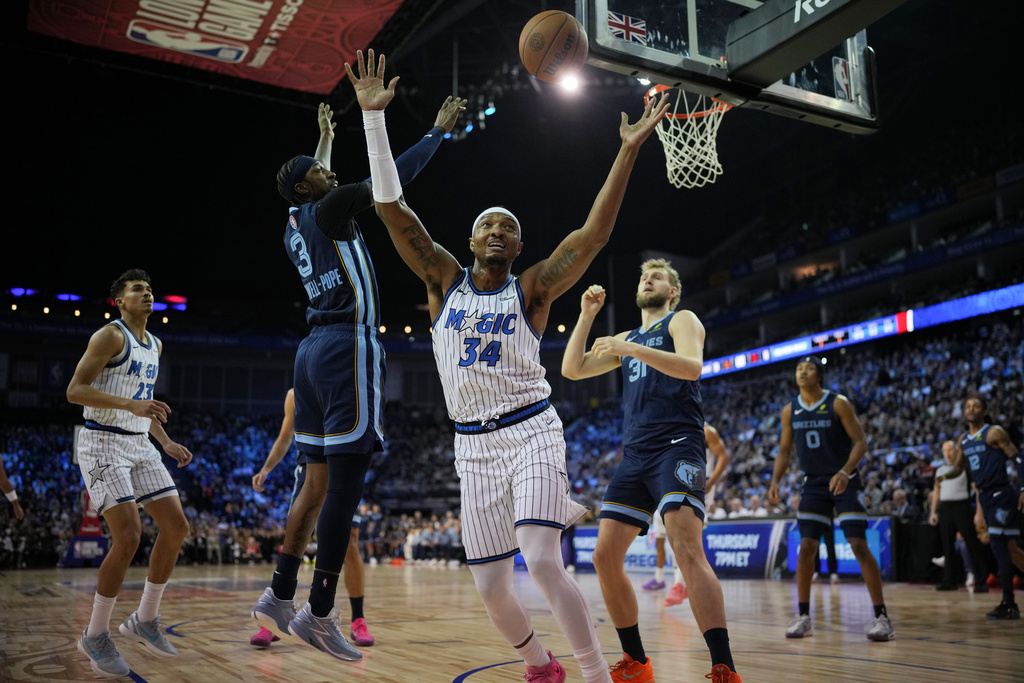 Orlando Magic center Wendell Carter Jr. (34) reaches for the ball as Memphis Grizzlies guard Kentavious Caldwell-Pope (3) and Memphis Grizzlies center Jock Landale (31) look on during the first half of NBA basketball game Sunday, Jan. 18, 2026, in London. (AP Photo/Kin Cheung)