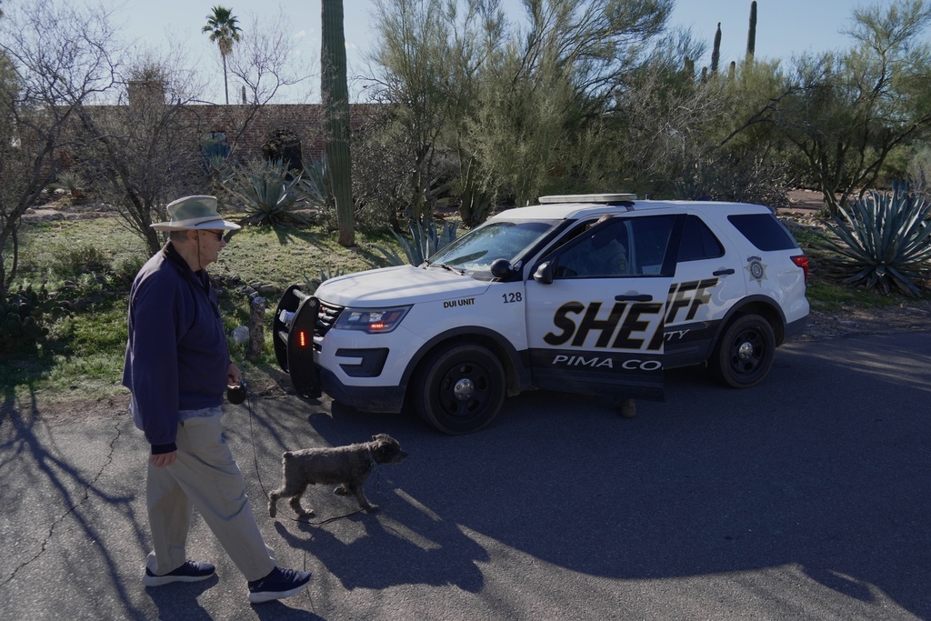 A person walks a dog as members of the Pima County sheriffs office remains outside of Nancy Guthrie's home, Monday, Feb. 9, 2026 in Tucson, Ariz. (AP Photo/Ty ONeil)