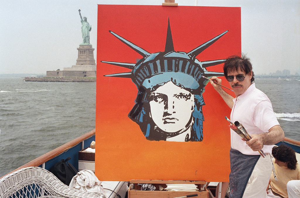 FILE - Artist Peter Max works on a painting of the Statue of Liberty aboard a boat in New York Harbor, July 4, 1987, in New York. (AP Photo/David Bookstaver, File)