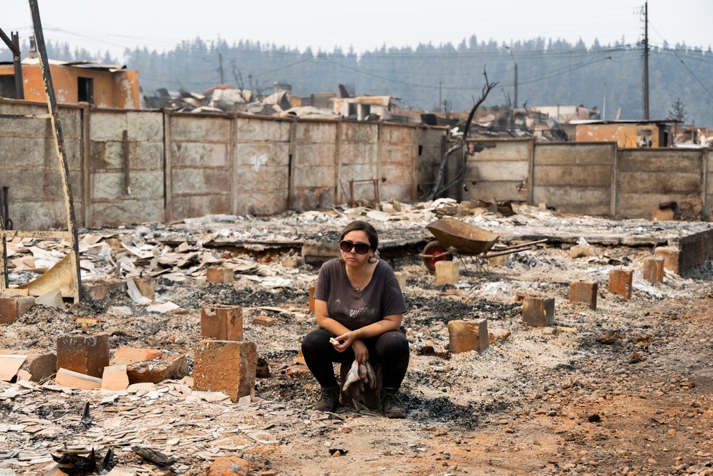 A woman sits on what remains of her home after it burned in wildfires in Punta de Parra, Chile, Monday, Jan. 19, 2026. (AP Photo/Javier Torres)