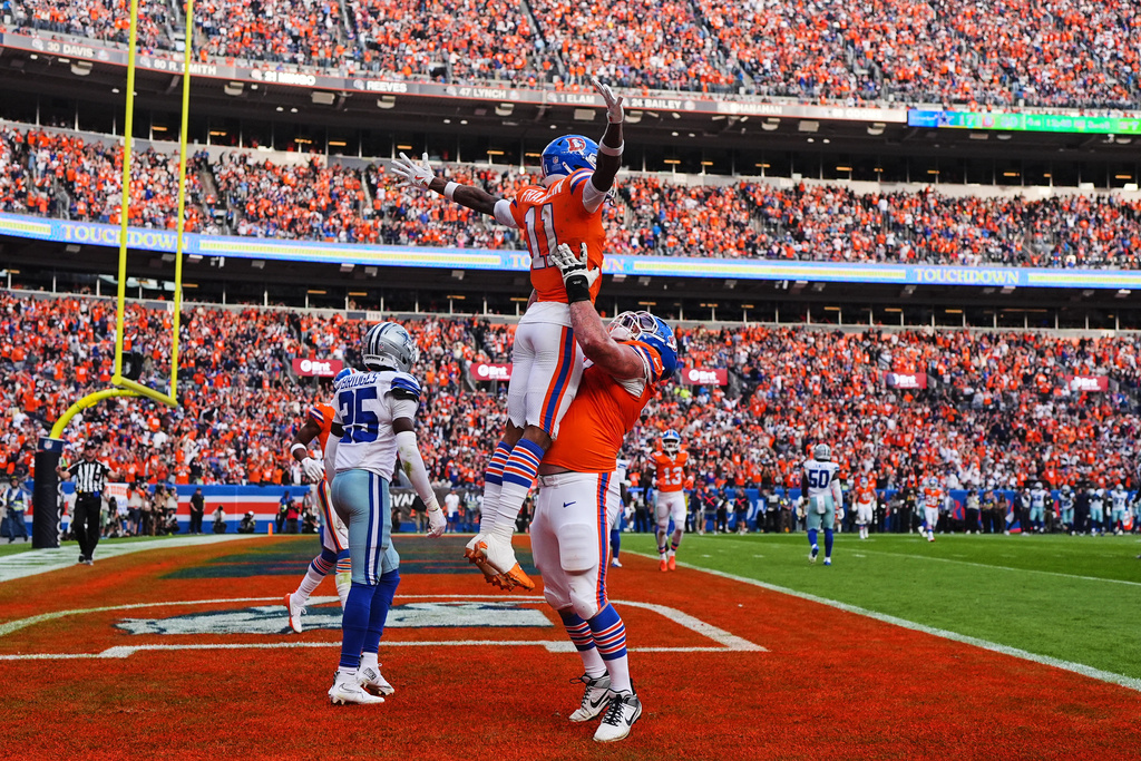 Denver Broncos' Garett Bolles, right, lifts Troy Franklin (11) as they celebrate Franklin's touchdown catch as Dallas Cowboys' Trikweze Bridges (25) walks away in the second half of an NFL football game Sunday, Oct. 26, 2025, in Denver. (AP Photo/Jack Dempsey)