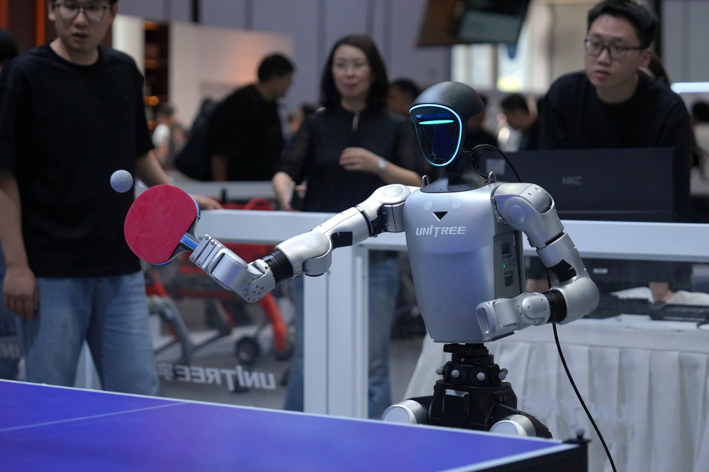 Exhibitors watch a robot play table tennis at a booth of Unitree, one of China's largest humanoid robot makers, during the World Robot Conference at the Beijing Yichuang International Convention and Exhibition Centre in Beijing, Wednesday, Aug. 19, 2026. (AP Photo/Andy Wong)