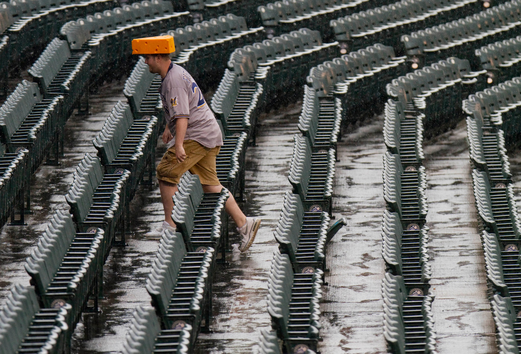 FILE - A fan wearing a cheesehead hat walks up the rain-soaked stands before a baseball game between the Milwaukee Brewers and the Colorado Rockies, July 14, 2011, in Denver. (AP Photo/Barry Gutierrez, File)