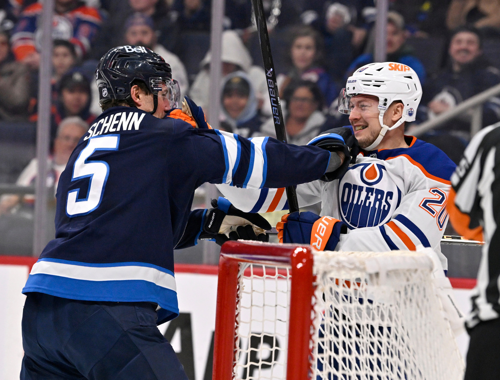 Edmonton Oilers' Curtis Lazar (20) and Winnipeg Jets' Luke Schenn (5) grab each other after a whistle during the first period of their NHL hockey game, in Winnipeg, Manitoba, Monday, Dec. 29, 2025. (Fred Greenslade/The Canadian Press via AP)