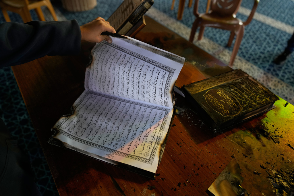 A boy inspects burnt copies of Quran inside a mosque that was torched and defaced by Israeli settlers overnight, in the West Bank town of Deir Istiya Thursday, Nov. 13, 2025. (AP Photo/Nasser Nasser)