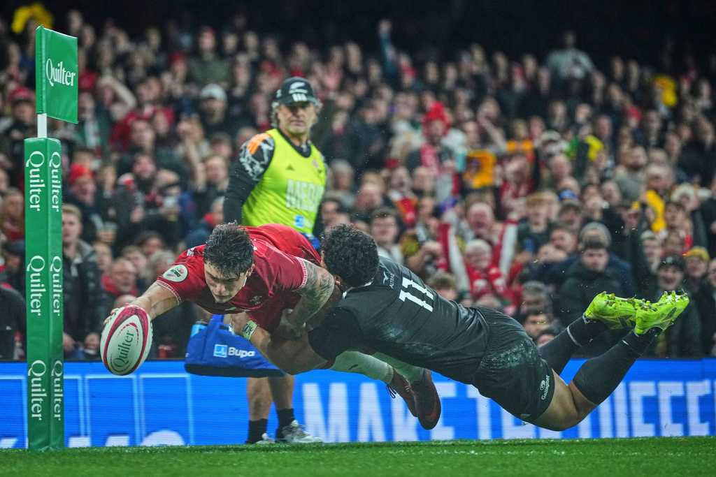 Wales' Louis Rees-Zammit dives over to score a try despite the challenge of New Zealand's Caleb Clarke during the Nation's Series rugby union international between Wales and New Zealand in Cardiff, Wales, Saturday, Nov. 22, 2025. (AP Photo/Alastair Grant)