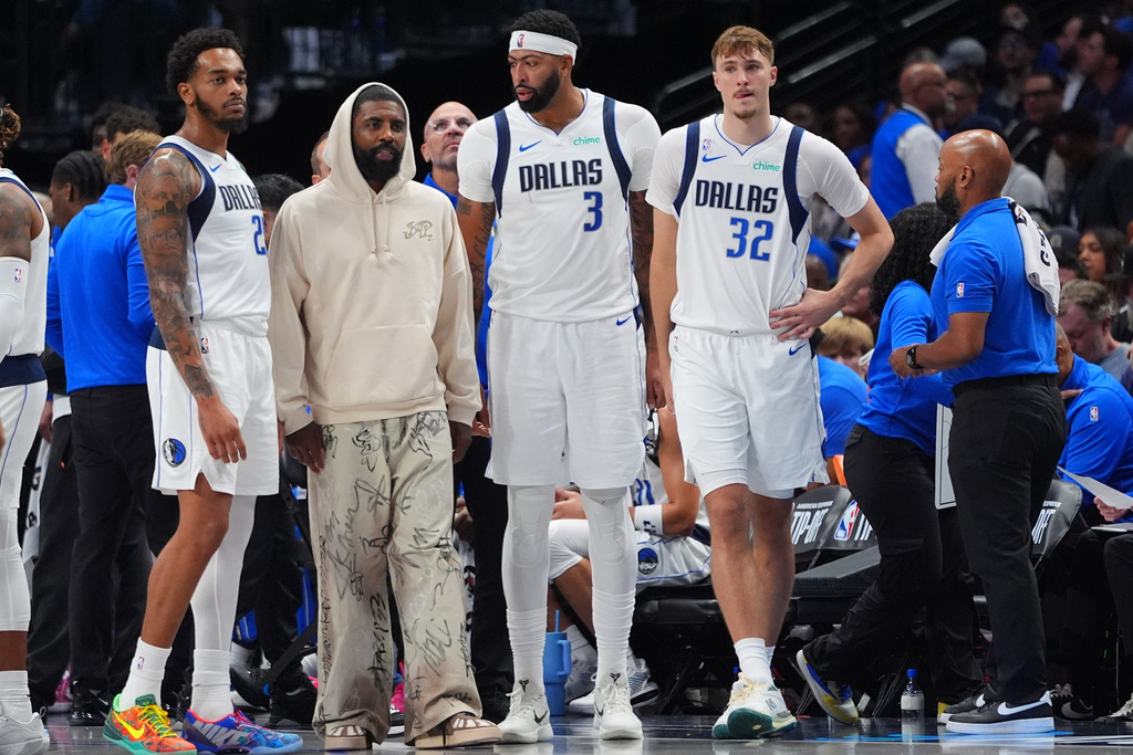 Dallas Mavericks teammates Cooper Flagg (32), Anthony Davis (3), Kyrie Irving, second from left, and P.J. Washington (25) look on from the bench area during a timeout in the second half of an NBA basketball game against the San Antonio Spurs in Dallas, Wednesday, Oct. 22, 2025. (AP Photo/LM Otero)