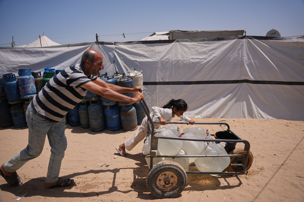 Ne'man Abu Jarad and his daughter push a cart loaded with jerrycans filled with water as they walk at a tent camp for displaced Palestinians in Khan Younis, southern Gaza Strip, Wednesday, May 13, 2026. (AP Photo/Abdel Kareem Hana)