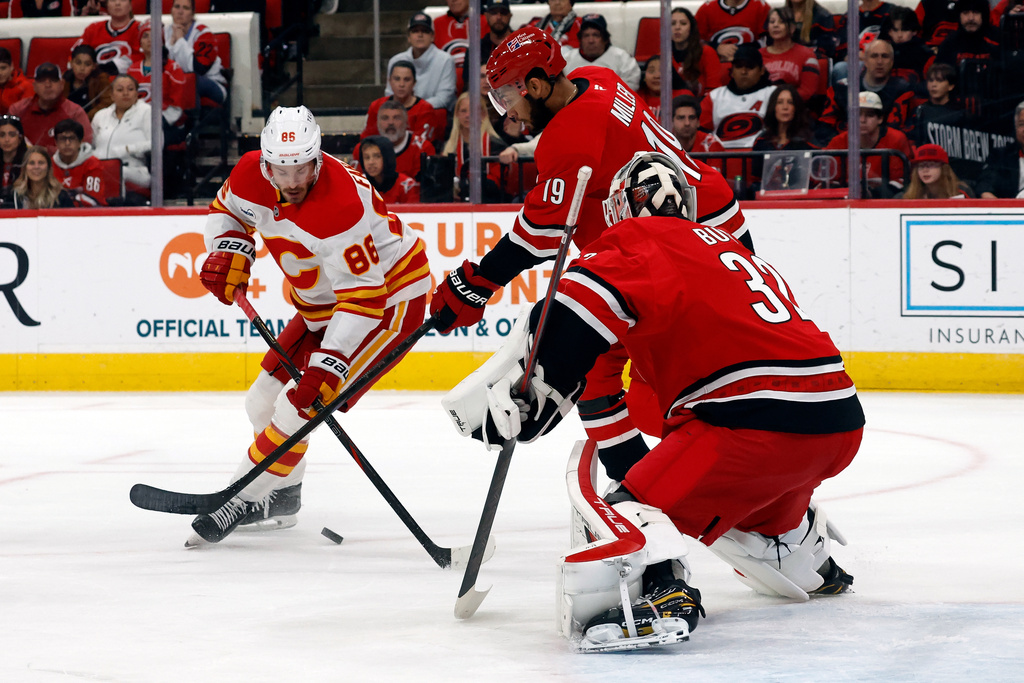 Carolina Hurricanes' K'Andre Miller (19) strips the puck from Calgary Flames' Joel Farabee (86) in front of Carolina Hurricanes goaltender Brandon Bussi, right, during the first period of an NHL hockey game in Raleigh, N.C., Sunday, Nov. 30, 2025. (AP Photo/Karl DeBlaker)