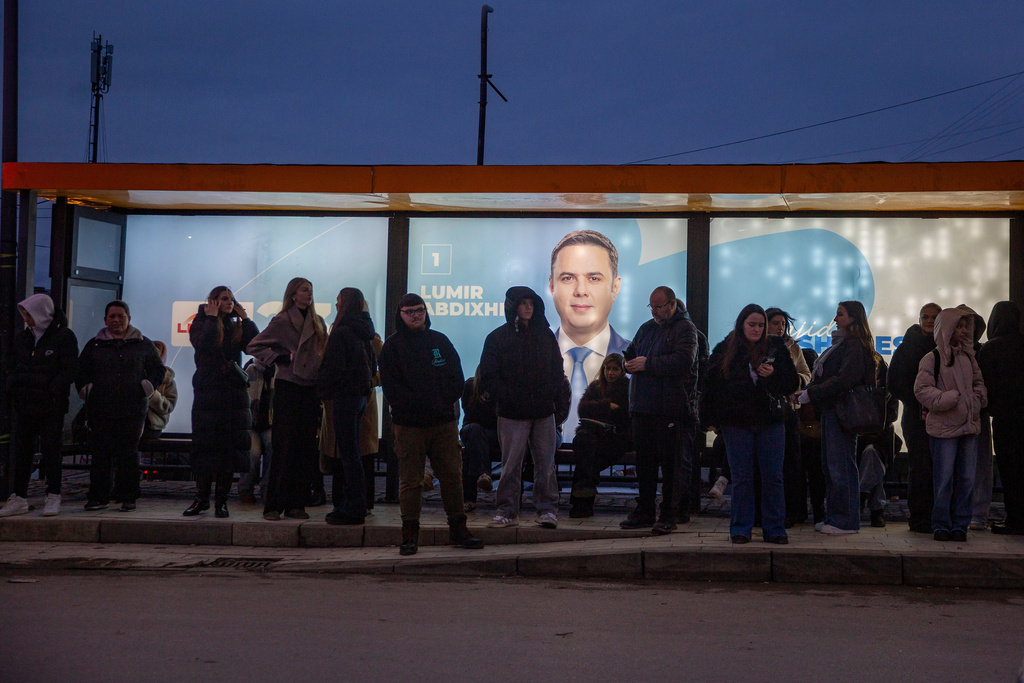 People waiting in the iluminated bus station with banners of LDK (Democratic League of Kosovo) leader Lumir Abdixhiku in capital Pristina on Thursday, Dec. 25, 2025. (AP Photo/Visar Kryeziu)
