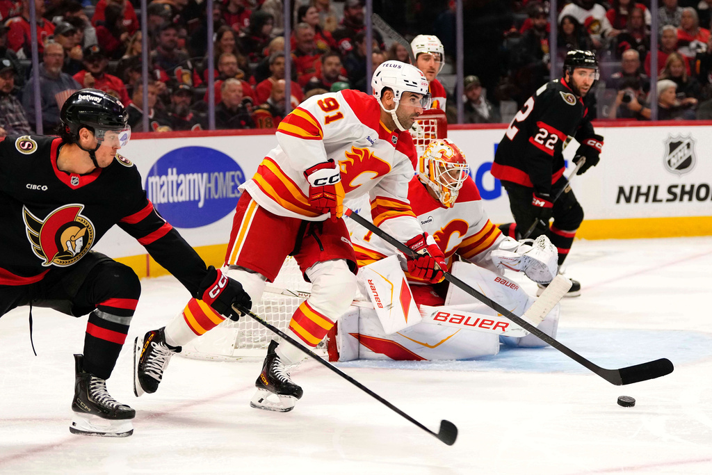 Calgary Flames' Nazem Kadri (91) gets the puck out of the Flames end as Ottawa Senators' Shane Pinto (12) chases, during second period NHL hockey action in Ottawa, on Thursday, Oct. 30, 2025. (Justin Tang/The Canadian Press via AP)