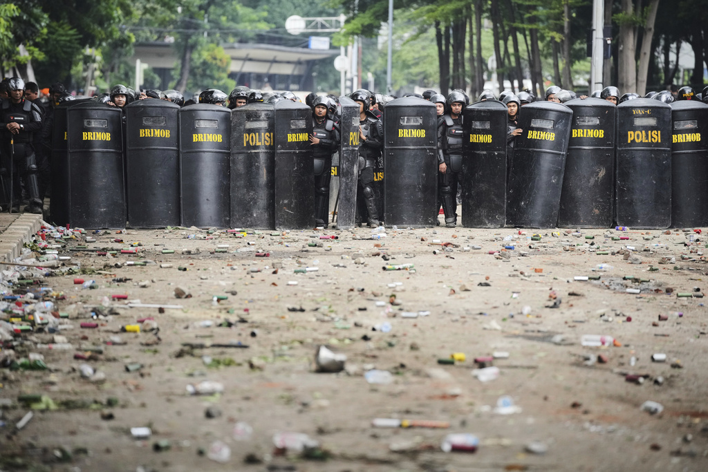 Debris litter the street as police officers take their position following violent protests against lawmakers' allowance and police brutality after a delivery rider was allegedly run over by a police armored vehicle during clashes between riot police and students protesters, in Jakarta, Indonesia, Saturday, Aug. 30, 2025. (AP Photo/Dita Alangkara)