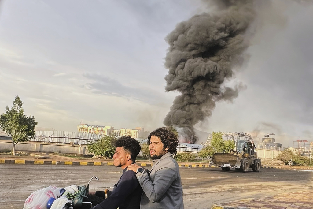 People ride a motorbike as smoke billows following Israeli airstrikes on multiple areas including a power planet and a gas station in Sanaa, Yemen, Sunday, Aug. 24, 2025. (AP Photo)