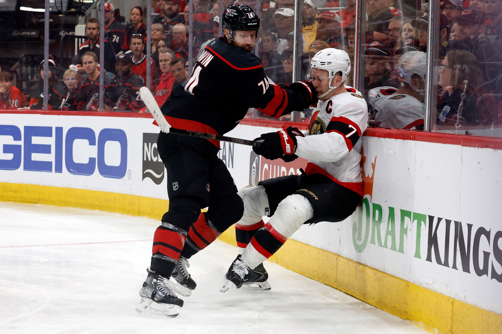 Carolina Hurricanes' Jaccob Slavin, left, checks Ottawa Senators' Brady Tkachuk (7) into the boards during the second overtime of Game 2 of an NHL hockey Stanley Cup first-round playoff series in Raleigh, N.C., Monday, April 20, 2026. (AP Photo/Karl DeBlaker)