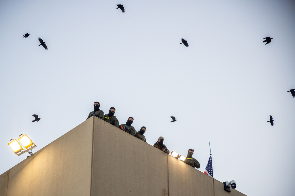 Police and federal officers stand guard on the roof of the U.S. Immigration and Customs Enforcement facility in Portland, Ore., Sunday, Oct. 5, 2025. (AP Photo/Ethan Swope)