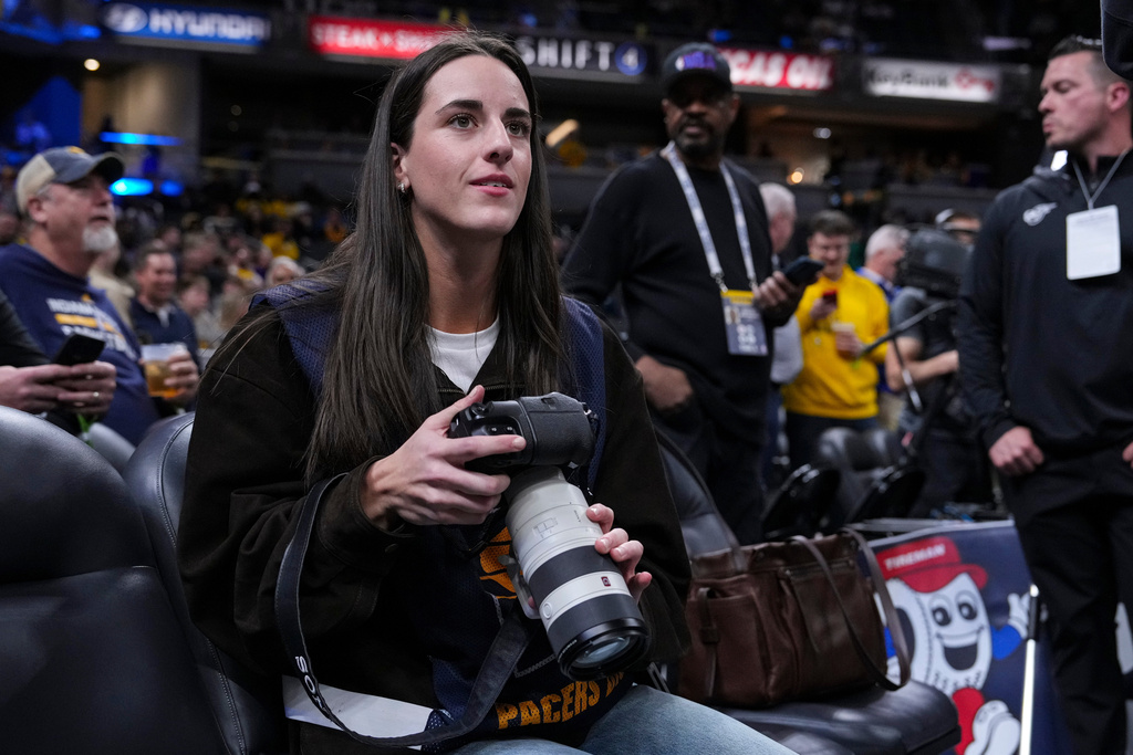 Indiana Fever guard Caitlyn Clark takes photos during pregame before an NBA basketball game between the Indiana Pacers and the Los Angeles Lakers in Indianapolis, Wednesday, March 25, 2026. (AP Photo/Michael Conroy)