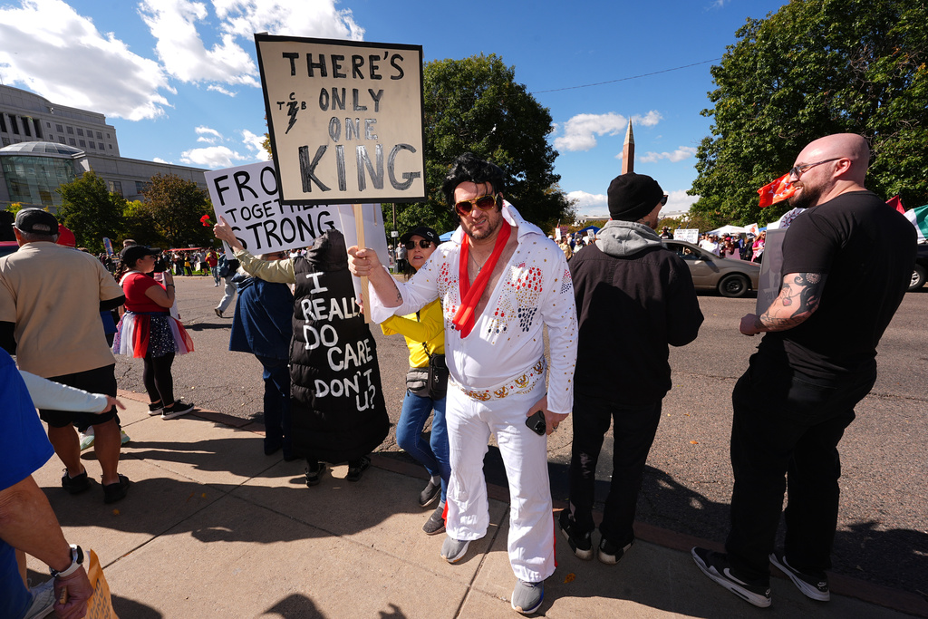 A rallygoer in a costume portraying singer Elvis Presley waves a placard during a rally and march through the streets in Denver, on Saturday, Oct. 18, 2025. (AP Photo/David Zalubowski)