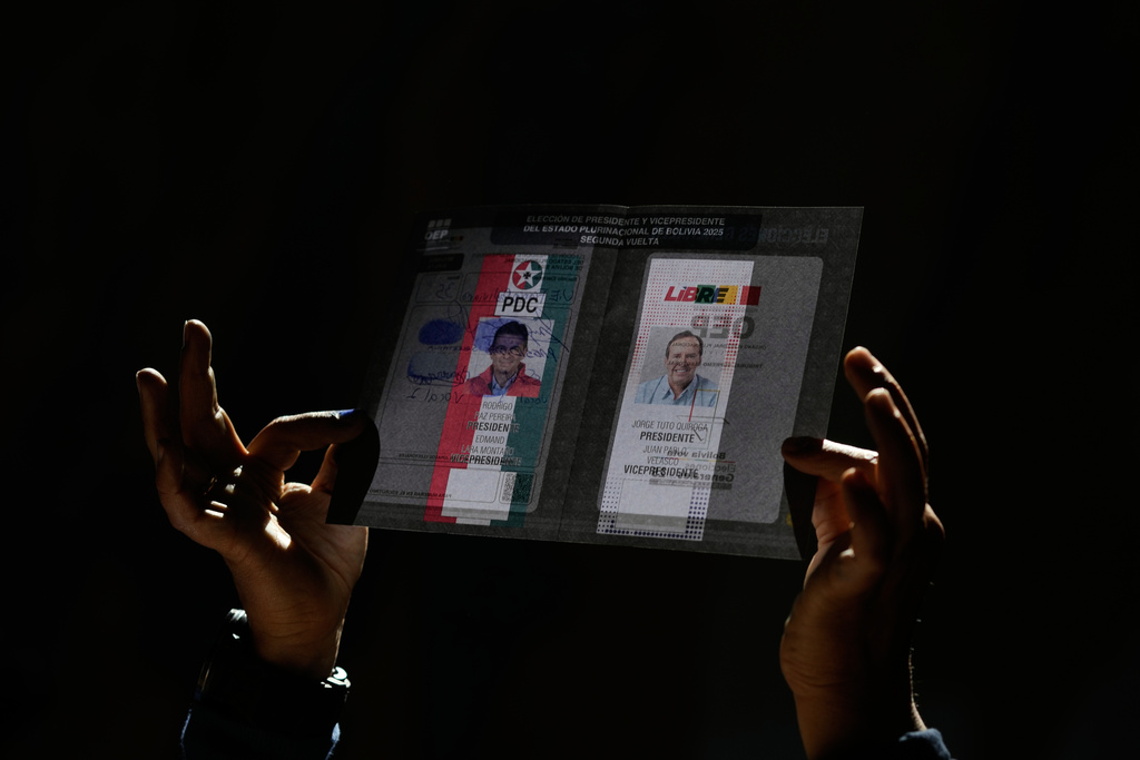 An electoral official shows an unmarked ballot with presidential candidates Jorge Quiroga, right, and Rodrigo Paz to voters during a runoff election in La Paz, Bolivia, Sunday, Oct. 19, 2025. (AP Photo/Natacha Pisarenko)