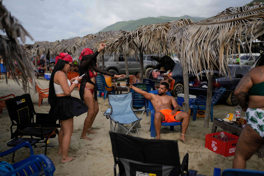 David Rodriguez hands a drink to his girlfriend on a beach in La Guaira, Venezuela, June 24, 2025. He traveled by land from Caracas to the U.S. border, crossing the Darien Gap, but was deported to Mexico by U.S. authorities and eventually gave up his hopes of reaching the United States, returning home. (AP Photo/Matias Delacroix)