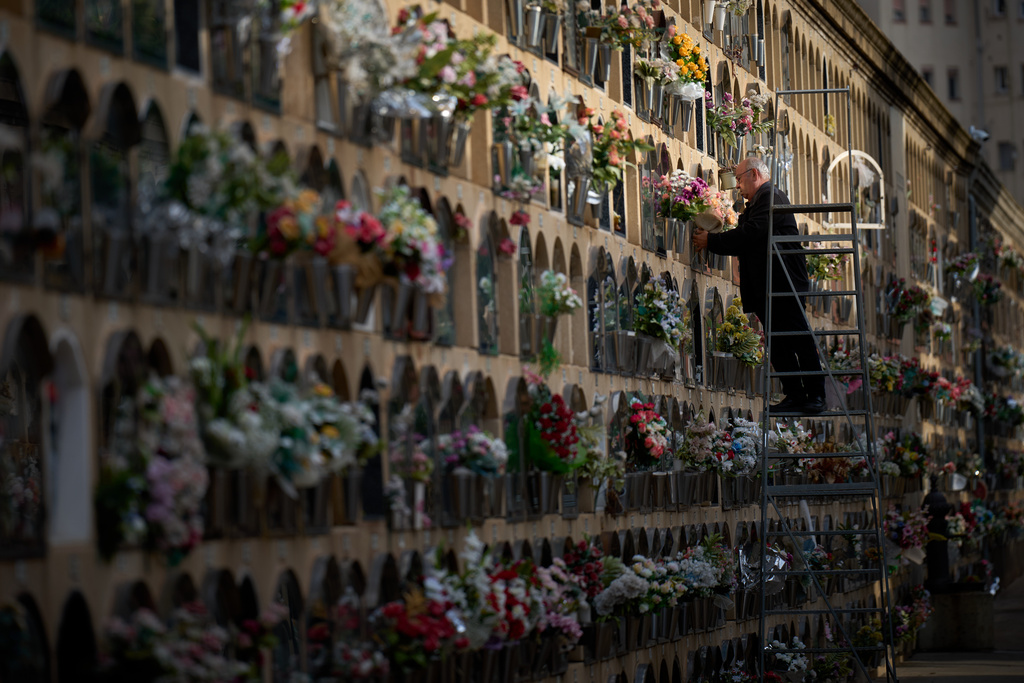 A man places flowers on a grave on All Saints' Day, a Catholic holiday to honor saints and remember deceased relatives, at a municipal cemetery in Barcelona, Spain, Saturday, Nov. 1, 2025. (AP Photo/Emilio Morenatti)