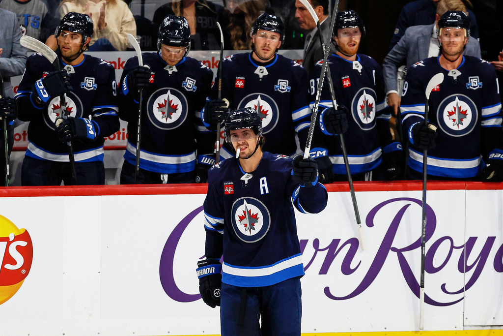 Winnipeg Jets' Mark Scheifele (55) raises his stick to the crowd as he is announced as franchise point leader during the first period of an NHL hockey game in Winnipeg, Manitoba, on Saturday, October 18, 2025. (John Woods/The Canadian Press via AP)