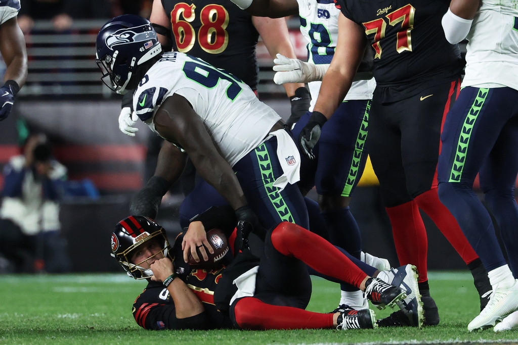 San Francisco 49ers quarterback Brock Purdy, bottom, reacts after being sacked by Seattle Seahawks defensive tackle Jarran Reed, middle, during the second half of an NFL football game in Santa Clara, Calif., Saturday, Jan. 3, 2026. (AP Photo/Jed Jacobsohn)