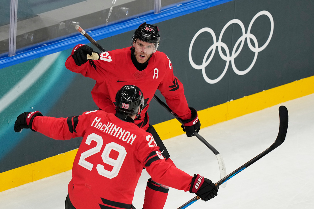 Canada's Connor McDavid, back, celebrates with Canada's Nathan MacKinnon after scoring his sides first goal during a preliminary round match of men's ice hockey between Canada and Switzerland at the 2026 Winter Olympics, in Milan, Italy, Friday, Feb. 13, 2026. (AP Photo/Hassan Ammar)