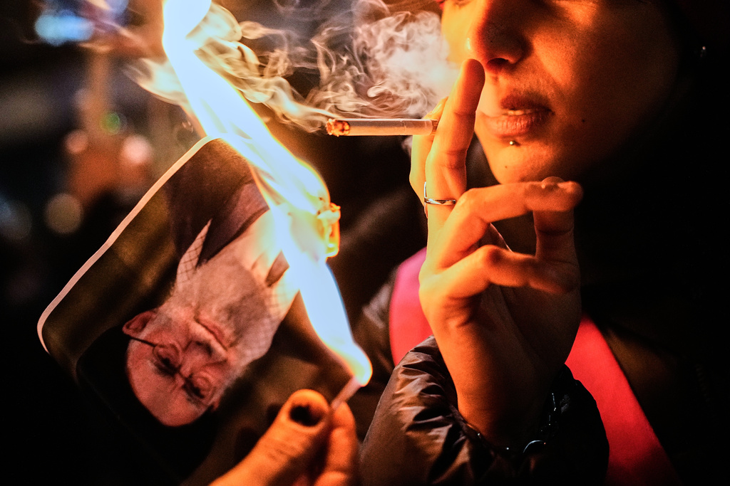 A protester smokes a cigarette after lighting it off a burning poster of Iran's Supreme Leader Ayatollah Ali Khamenei during a demonstration in Berlin, Germany, in support of the nationwide mass protests in Iran against the government, Wednesday, Jan. 14, 2026. (AP Photo/Ebrahim Noroozi)