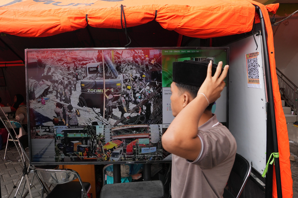 A student walks pas a TV screen showing the search efforts for the missing people of a building that collapsed at an Islamic boarding school in Sidoarjo, East Java, Indonesia, Saturday, Oct. 4, 2025. (AP Photo/Achmad Ibrahim)