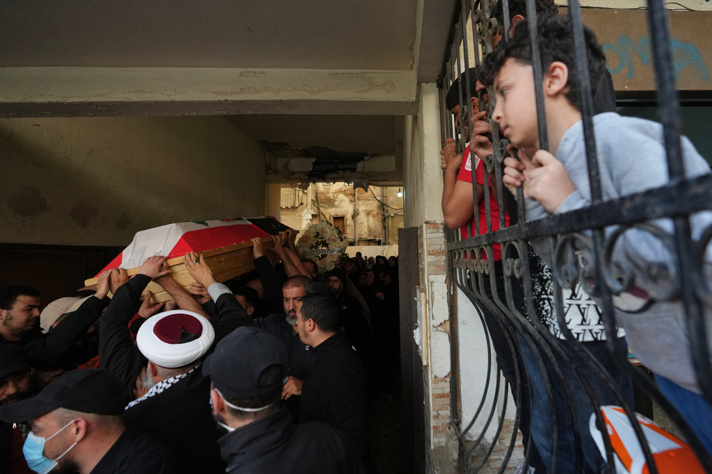 Mourners carry the coffin of Palestinian fighter Hozeifa Hamza Ghannamieh, who was killed alongside Ibrahim Anwar al-Khalayli while fighting alongside Hezbollah against Israel in southern Lebanon, during their funeral procession as children watch from behind a fence in Beirut, Lebanon, Tuesday, April 28, 2026. (AP Photo/Hassan Ammar)