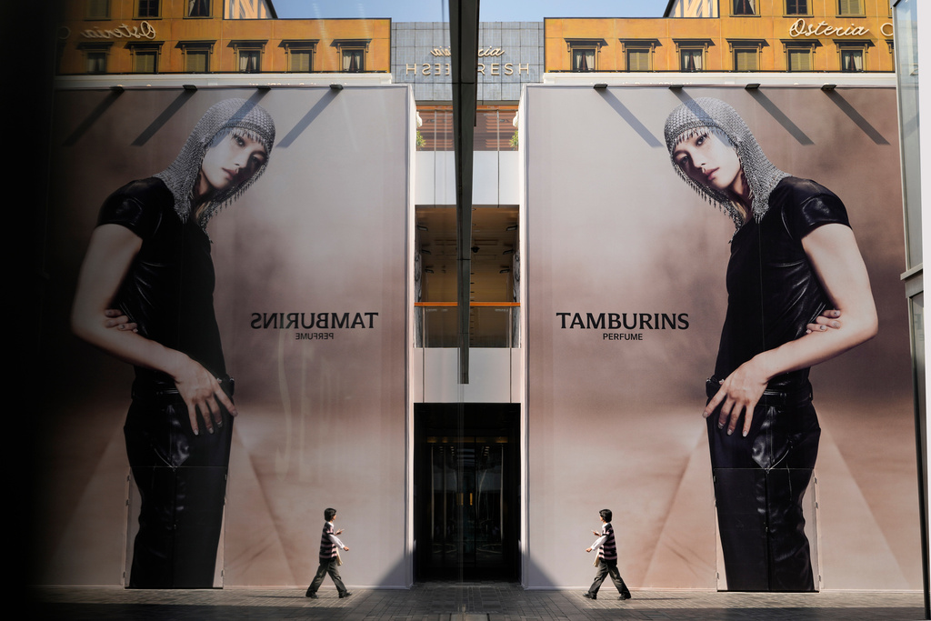 A shopper, right, walking under giant advertisements is reflected off the glass wall of a shop at a trendy shopping district during the National Day holidays in Beijing, China, Thursday, Oct. 2, 2025. (AP Photo/Ng Han Guan)