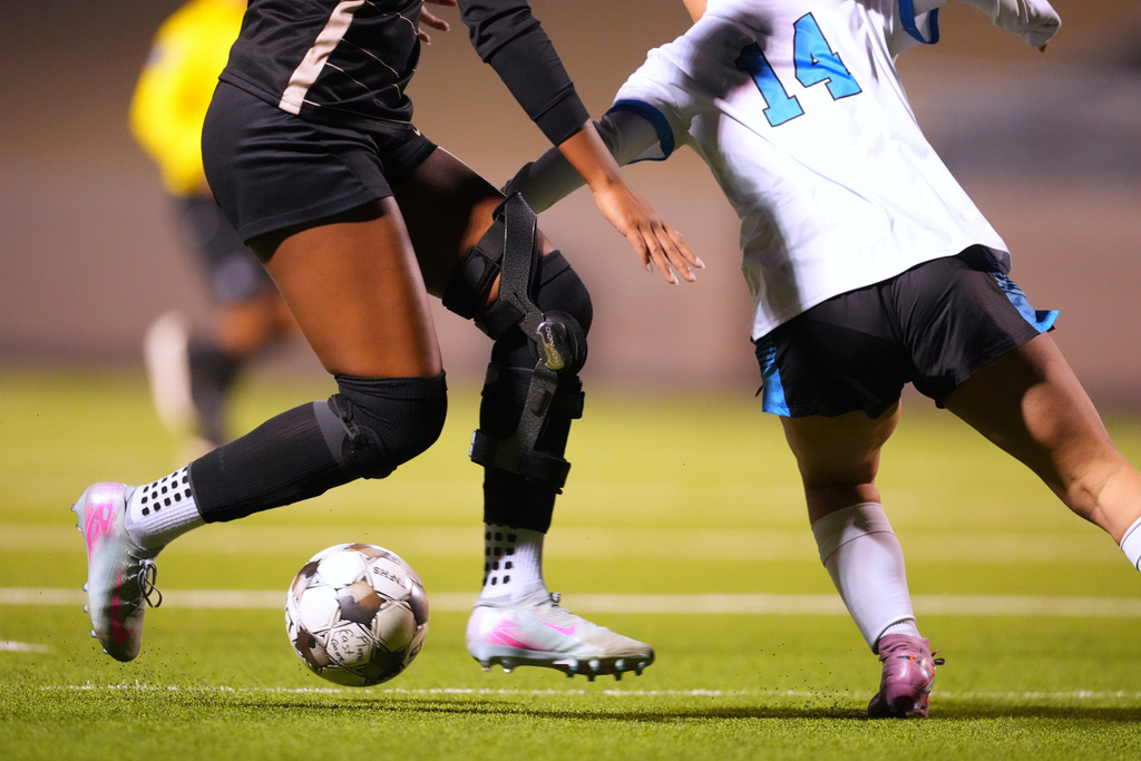 Plano East varsity soccer player Aliya Jacob's knee brace, left, is visible as she attacks Rock Hill's Adalina Flores during a soccer game, Jan. 30, 2026, in Murphy, Texas. (AP Photo/Julio Cortez)