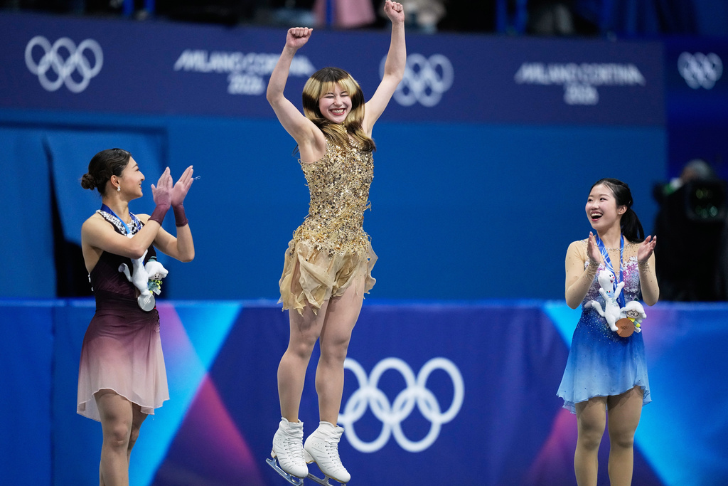 From left to right, silver medalist Kaori Sakamoto of Japan, gold medalist Alysa Liu of the United States, and bronze medalist Ami Nakai of Japan, jump on the podium to receive their medals after competing in the women's free skate program in figure skating at the 2026 Winter Olympics, in Milan, Italy, Thursday, Feb. 19, 2026. (AP Photo/Natacha Pisarenko)