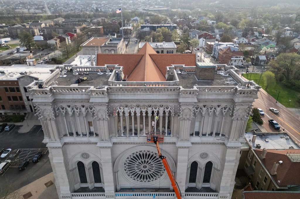 Workers are seen beyond an orange cherry picker high on the Cathedral Basilica of the Assumption, known as "America's Notre Dame," as the final new terra cotta gargoyle is secured with straps to the left, in Covington, Ky., on Tuesday, March 31, 2026. (AP Photo/Carolyn Kaster)