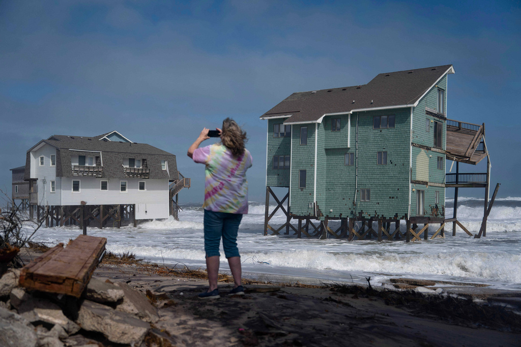 A person stands and takes photos of houses at risk of collapse in the midst of a storm, Sunday, Oct. 12, 2025, in Buxton, N.C. (AP Photo/Allison Joyce)