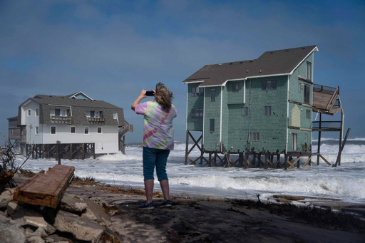 A person stands and takes photos of houses at risk of collapse in the midst of a storm, Sunday, Oct. 12, 2025, in Buxton, N.C. (AP Photo/Allison Joyce) A person stands and takes photos of houses at risk of collapse in the midst of a storm, Sunday, Oct. 12, 2025, in Buxton, N.C. (AP Photo/Allison Joyce)