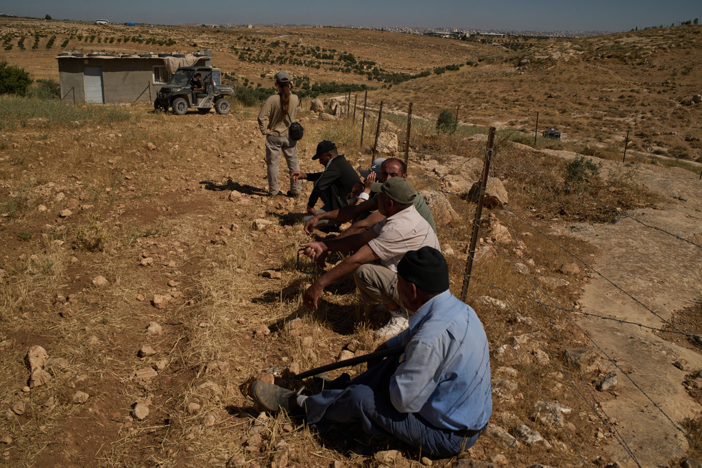 After Israeli soldiers told them to remain by the fence, Palestinians and an Israeli activist sit watching as settlers arrive in a vehicle after the settlers accused a local Palestinian resident of setting fire to a field, near the West Bank village of Susya in the Masafer Yatta region, Thursday, June 18, 2026. (AP Photo/Leo Correa)