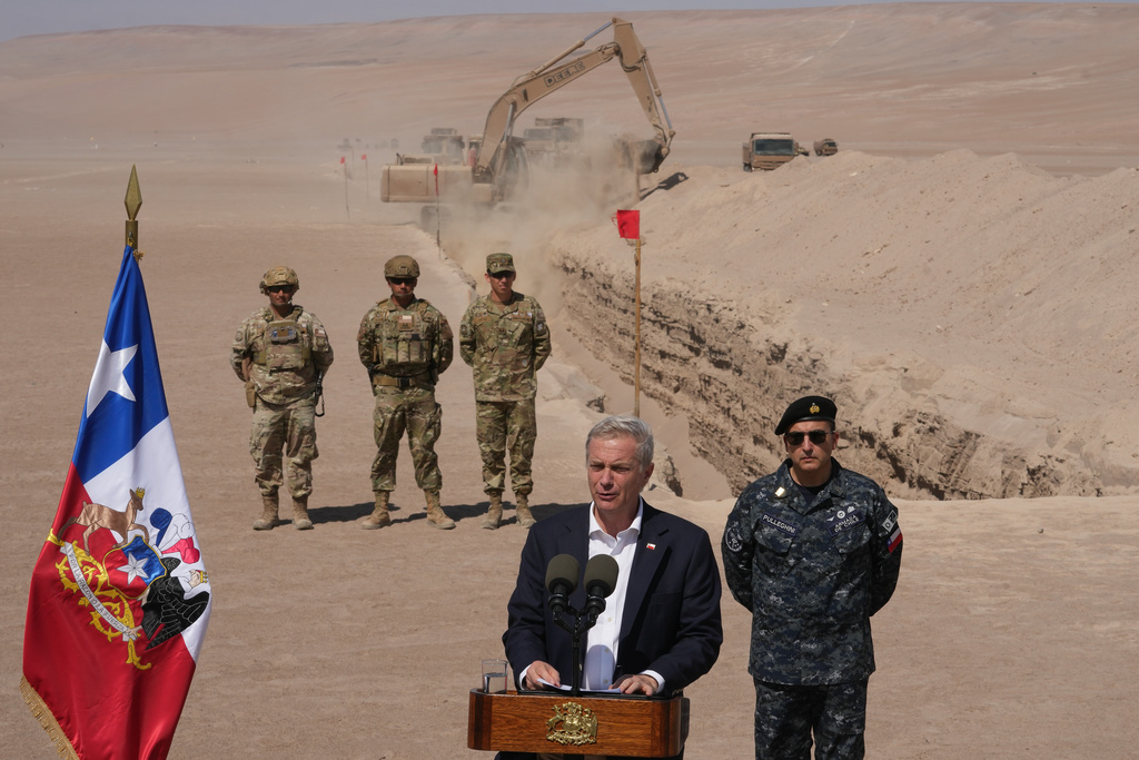 Chilean President Jose Antonio Kast gives a press conference as a machine digs, as part of measures to deter irregular migration, along the northern border at the Chacalluta border crossing, in Arica, Chile, Monday, March 16, 2026. (AP Photo/Esteban Felix)