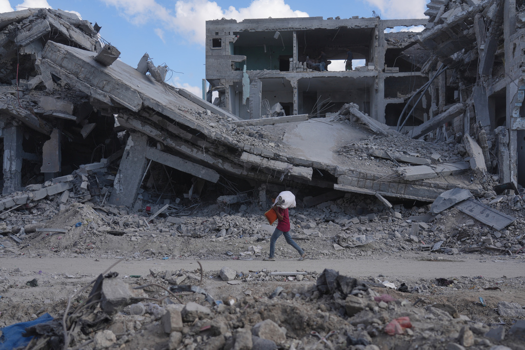 A Palestinian carries belongings while walking past destroyed buildings in Gaza City, Sunday, Oct. 12, 2025, after Israel and Hamas agreed to a pause in their war and the release of the remaining hostages. (AP Photo/Jehad Alshrafi)