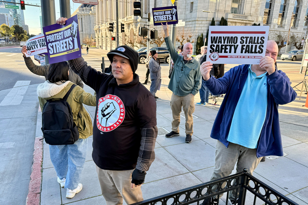 Demonstrators holds signs during a protest by Uber and Lyft drivers asking state regulators to take self-driving taxis off the streets due to safety concerns at the California Public Utilities Commission headquarters Friday, Jan. 9, 2026, in San Francisco. (AP Photo/Haven Daley)