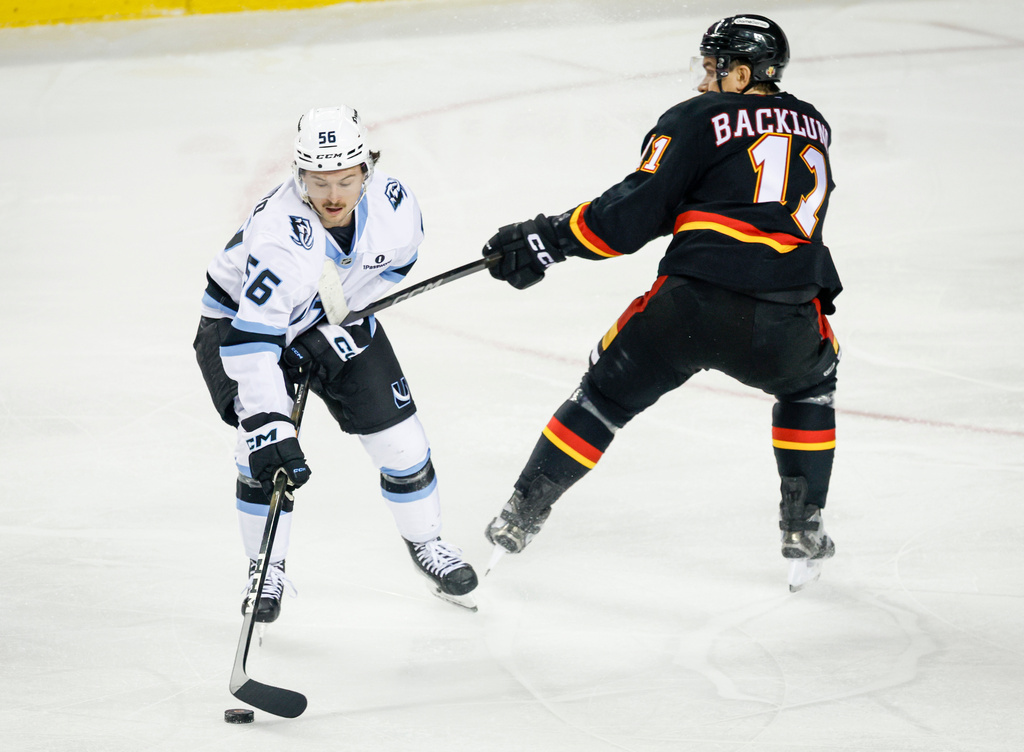 Utah Mammoth's Kailer Yamamoto, left, is hit on the chest by the stick of Calgary Flames' Mikael Backlund, right, during first-period NHL hockey game action in Calgary, Alberta, Saturday, Dec. 6, 2025. (Jeff McIntosh/The Canadian Press via AP)