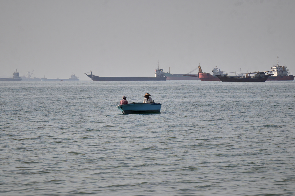 Two men sit in a small boat on the water as a mix of bulk carriers, cargo ships, and service vessels line the horizon in the Strait of Hormuz off Bandar Abbas, Iran, Monday, April 27, 2026.(Razieh Poudat/ISNA via AP)